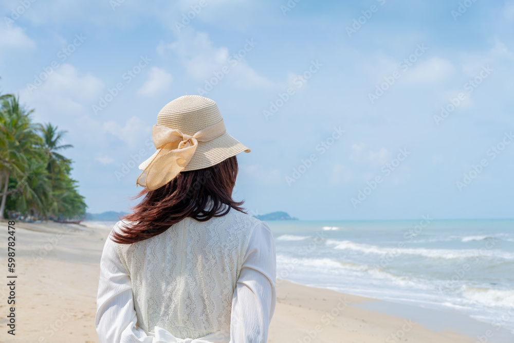 Happy Young woman in a white dress and hat standing on the beach and enjoying freedom, and looking at the sea.