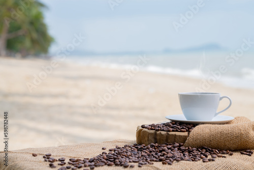 Close-up white coffee cup and many coffee beans placed around on the wood table with a beautiful seascape of nature background, concept coffee vacation travel.