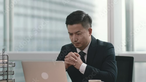 mid adult asian businessman working in office using laptop computer photo