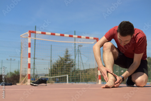 Mature adult doing sport is touching damaged articulation, barefoot. The other leg is knee down. Copy space colorful picture. Sports physiotherapy concept. High quality photo