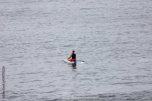 A person kneeling on a paddle board in the ocean in La Jolla Cove in California.