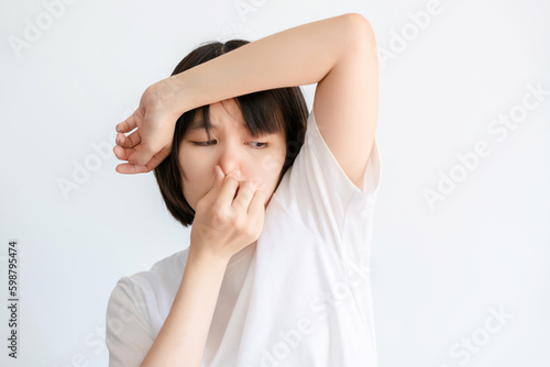 A woman wearing a white t-shirt expressing disgust at the smell of her armpits.