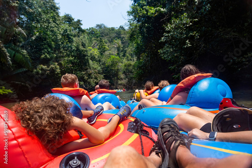 Large group of people floating down a scenic jungle river in Belize Central America on a natural Cave Tubing adventure. Real people having real outdoor fun in the jungle. View from behind