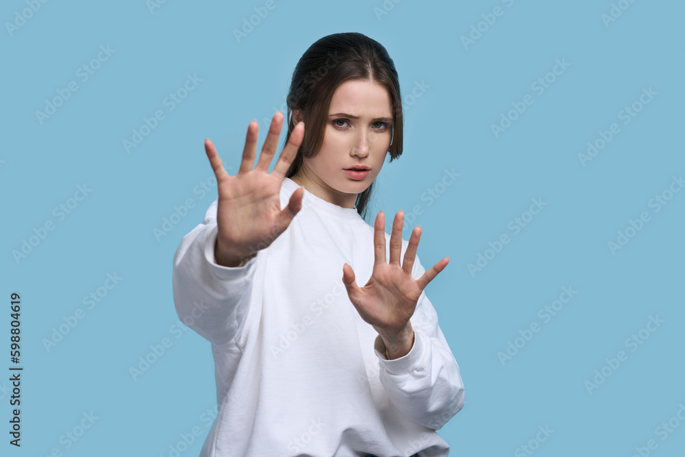 Worried Caucasian young woman shows stop sign, expressing misunderstanding and denial, blue backdrop Worried Caucasian young woman shows stop sign, expressing misunderstanding and denial, blue backdrop