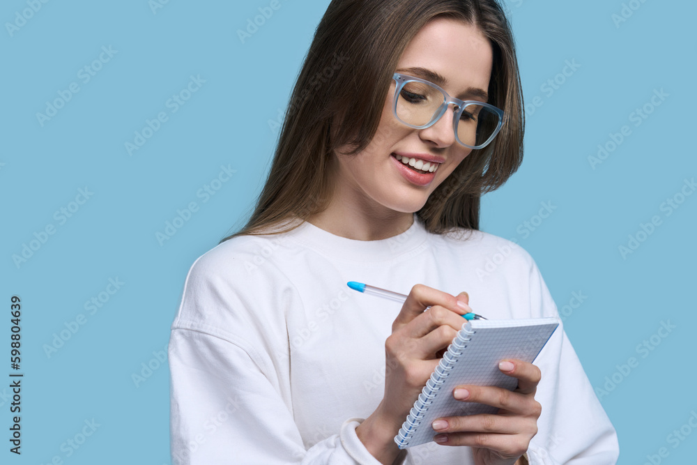 Charming Caucasian young woman in stylish blue framed eyeglasses, taking notes over blue background Charming Caucasian young woman in stylish blue framed eyeglasses, taking notes over blue background