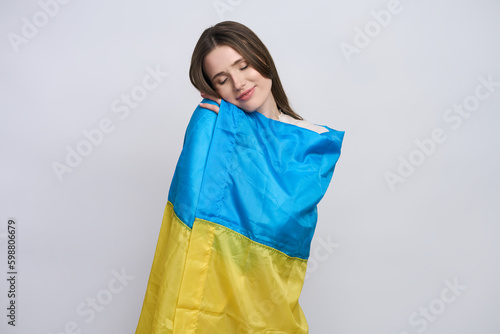 Beautiful Ukrainian young patriotic woman wrapped in Ukraine flag, smiling, isolated white backdrop
