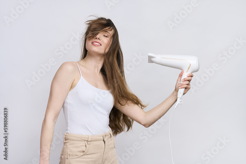 Attractive young woman with beautiful shiny long hair, using hair dryer isolated on white background