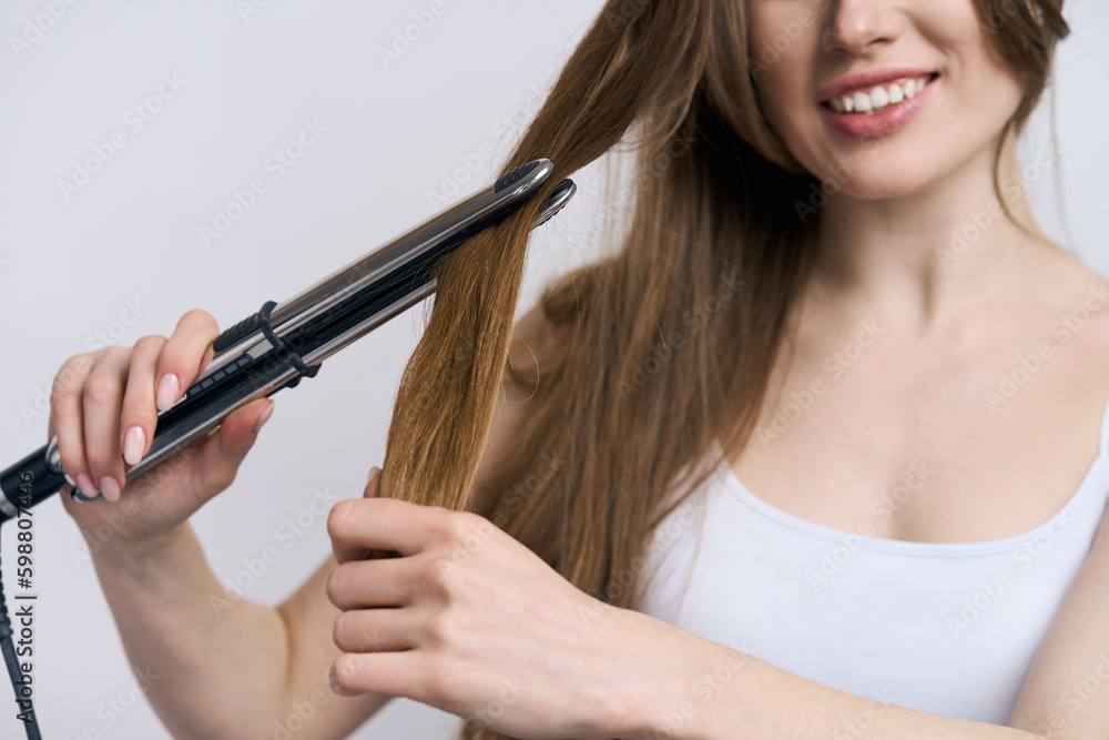 Selective focus on modern electric hair straightener in hands of smiling woman straightening hair