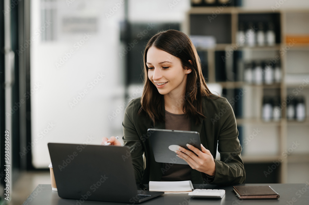 Beautiful woman using laptop and tablet while sitting at her working place. Concentrated at work. Beautiful woman using laptop and tablet while sitting at her working place. Concentrated at work.