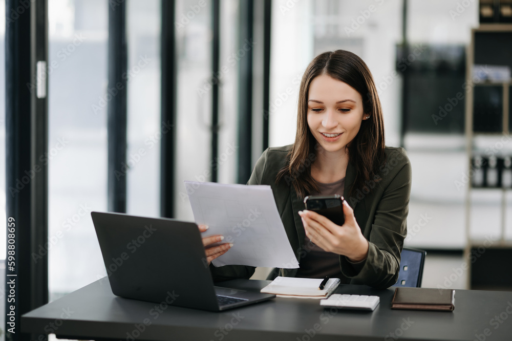 Business Caucasian woman Talking on the phone and using a laptop with a smile while sitting at modern office Business Caucasian woman Talking on the phone and using a laptop with a smile while sitting at modern office