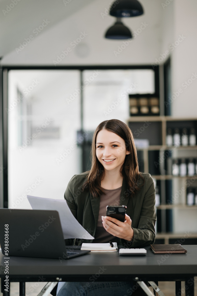 Business Caucasian woman Talking on the phone and using a laptop with a smile while sitting at modern office Business Caucasian woman Talking on the phone and using a laptop with a smile while sitting at modern office