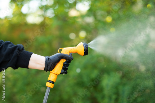 Working watering garden from hose. Hand with garden hose watering plants, close up, blurred background. Gardening concept