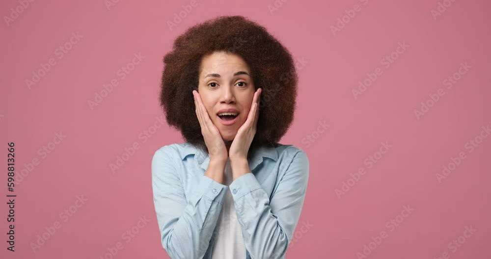shocked amazed African American woman with wide open mouth touching face in astonishment and wonder standing over pink studio background shocked amazed African American woman with wide open mouth touching face in astonishment and wonder standing over pink studio background