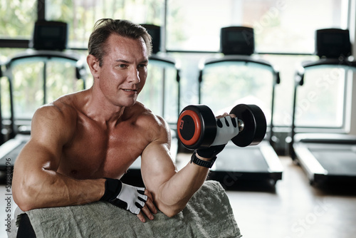 Smiling middle-aged man working out with heavy dumbbells, upper body workout concept