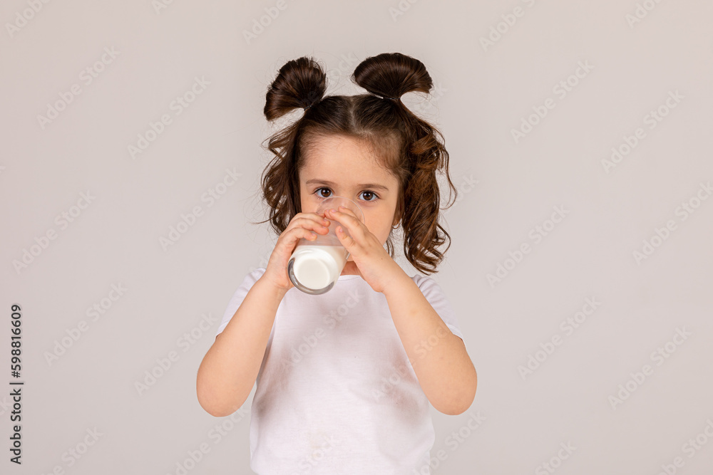 little cute brunette girl in white tank top drinking milk on a light background, space for text. healthy delicious breakfast little cute brunette girl in white tank top drinking milk on a light background, space for text. healthy delicious breakfast