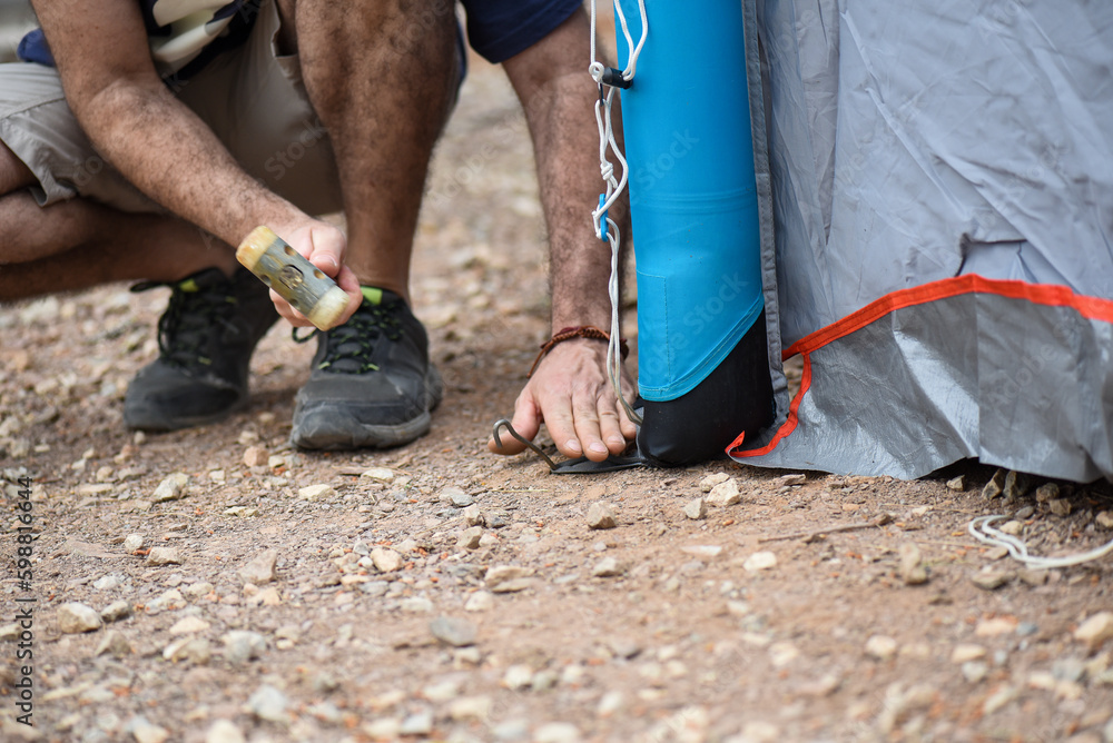 man pitching tent on campsite, detail video of hand and hammer clutching pickaxes in hard ground, caucasian man in his forties