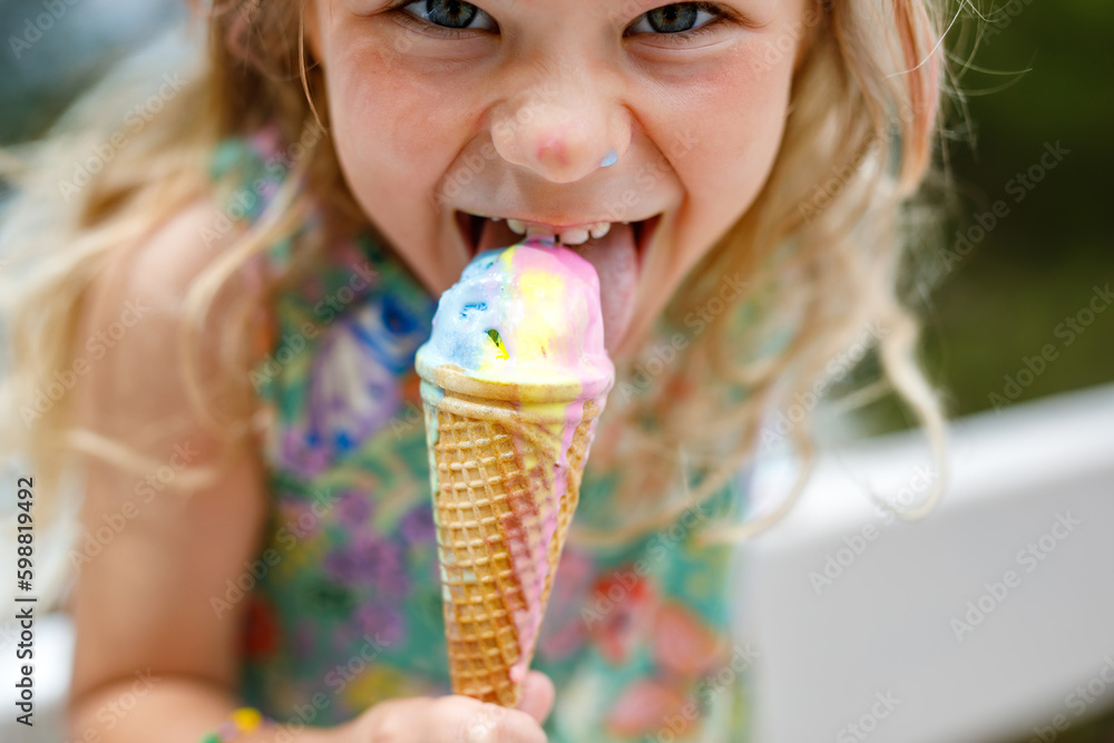 Happy preschool girl eating colorful ice cream in waffle cone on sunny summer day. Little toddler child eat icecream dessert. Sweet food on hot warm summertime days. Bright light, colorful ice-cream Happy preschool girl eating colorful ice cream in waffle cone on sunny summer day. Little toddler child eat icecream dessert. Sweet food on hot warm summertime days. Bright light, colorful ice-cream