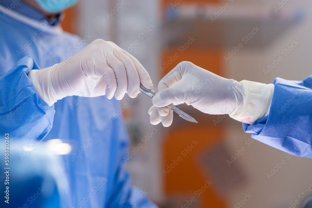 Team of surgery doctor in Operating Room hold hands scalpel surgical blade give to Surgeons During Operation. surgeons assistance in green gown coat give scalpel surgical blade to doctor Team of surgery doctor in Operating Room hold hands scalpel surgical blade give to Surgeons During Operation. surgeons assistance in green gown coat give scalpel surgical blade to doctor