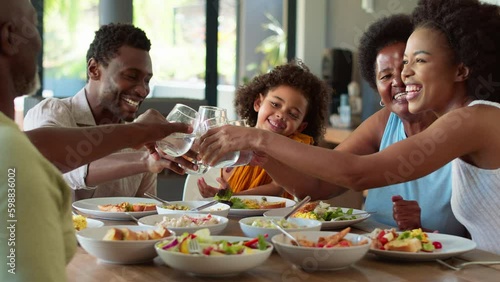 Multi-generation family sitting around table at home doing cheers with water glasses at meal - shot in slow motion