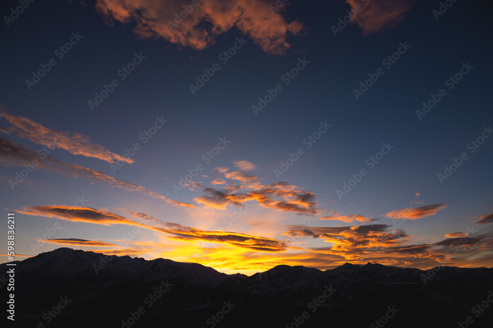 Colorful sunset over mountain hills. The black silhouette of the mountains is visible through the picturesque glow Colorful sunset over mountain hills. The black silhouette of the mountains is visible through the picturesque glow