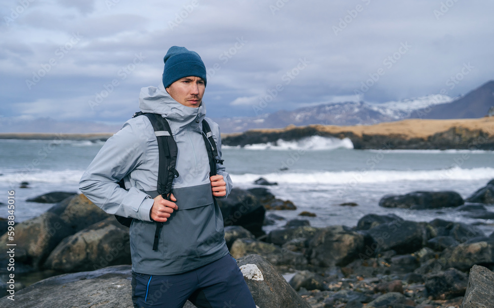 Side view of man in warm clothes during trip through Iceland. Backpacker travels to Iceland. Travel tourist in nature landscape. Active people on winter holidays.