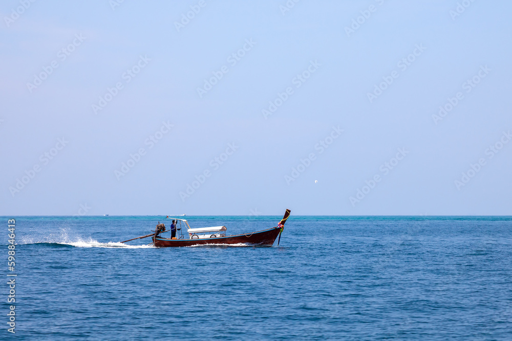 Old traditional Thai motorboat made of wood for fishing and transporting tourists on excursions in the Andaman Sea in clear turquoise water under a blue sky. Travel and vacation in phuket.