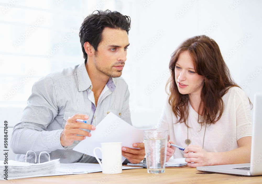 Making sure paper and online figures match. a two young design professionals sitting together and going over paperwork. Making sure paper and online figures match. a two young design professionals sitting together and going over paperwork.