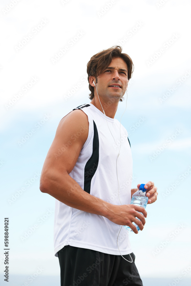 He has a strong motivation for physical fitness. Handsome young male holding a water bottle, listening to music and looking away after his morning run. He has a strong motivation for physical fitness. Handsome young male holding a water bottle, listening to music and looking away after his morning run.