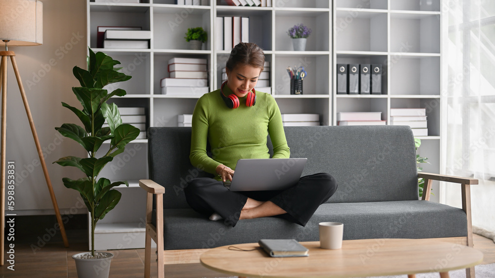Happy Asian woman using her laptop on a sofa in her living room. Happy Asian woman using her laptop on a sofa in her living room.
