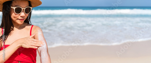 Beautiful young Asian woman apply sun protection on to her hand on tropical beach. Girl applying sun cream to her skin. UV protection, summer and holiday concept. Free space, closeup © Pattarisara