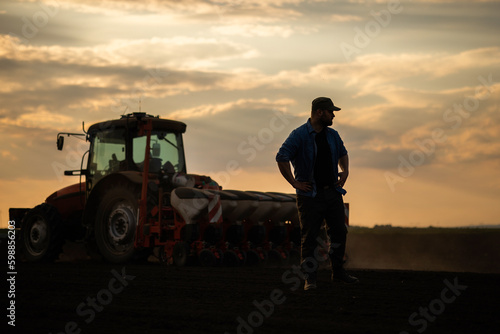  Satisfied tractor driver after work on agricultural field stands next to tractor.