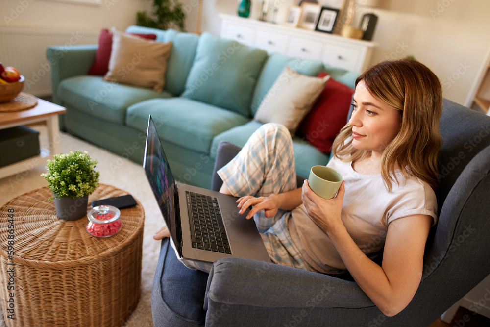 Young woman using a laptop at home while relaxing in armchair Young woman using a laptop at home while relaxing in armchair