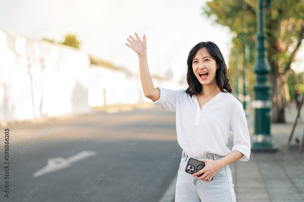 Portrait young beautiful asian woman waving hand to friend by the street in sunny holiday. Portrait young beautiful asian woman waving hand to friend by the street in sunny holiday.