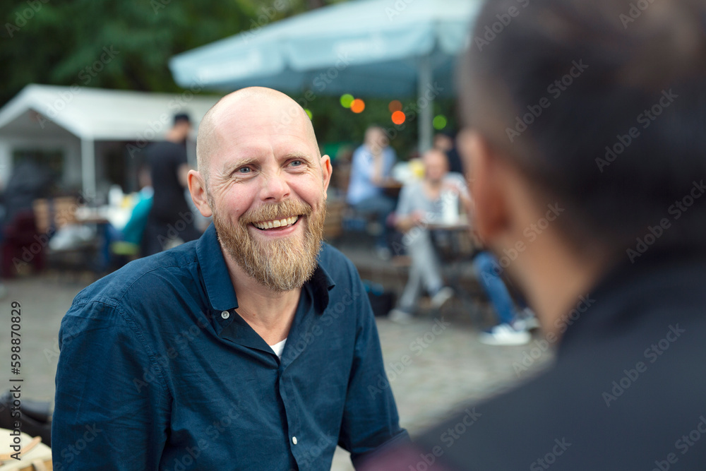 Smiling man talking to friend at sidewalk cafe Smiling man talking to friend at sidewalk cafe