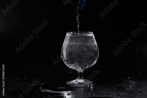 Pouring purified fresh water in glass on mirror background. Glass cup with water and bubbles on a black background