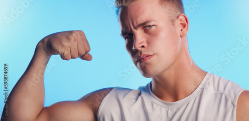 You want a piece of this. Studio portrait of a handsome young man flexing his bicep against a blue background.