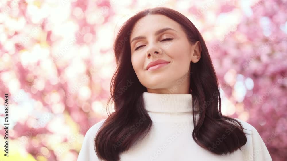 Stunning young dark haired woman take deep breath at the city street and enjoying beautiful day with sakura flowers in the background Pretty woman looking at pink blossom at spring morning outdoors Stunning young dark haired woman take deep breath at the city street and enjoying beautiful day with sakura flowers in the background Pretty woman looking at pink blossom at spring morning outdoors