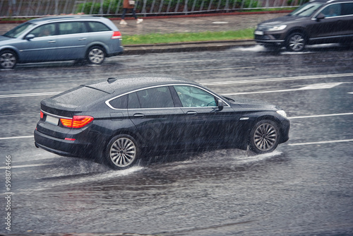 Obraz na płótnie Car driving fast on wet road, driving through puddle during heavy rain. Car driving on flooded asphalt road. Dangerous driving conditions, wet road risk of aquaplaning. Slippery road, low visibility w salonie
