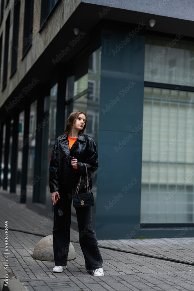 Young lady in leather jacket stand in urban city with credit card in hand.