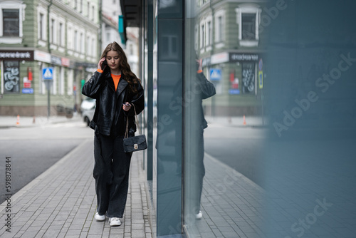 Young lady in leather jacket walking in urban city, speaking on phone.