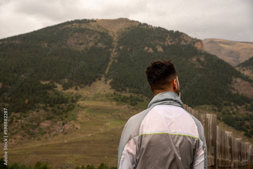 A young dark-haired man with his back turned and wearing a grey sweatshirt admiring the mountainous and natural landscape of Huesca in Aragon on a cloudy day.