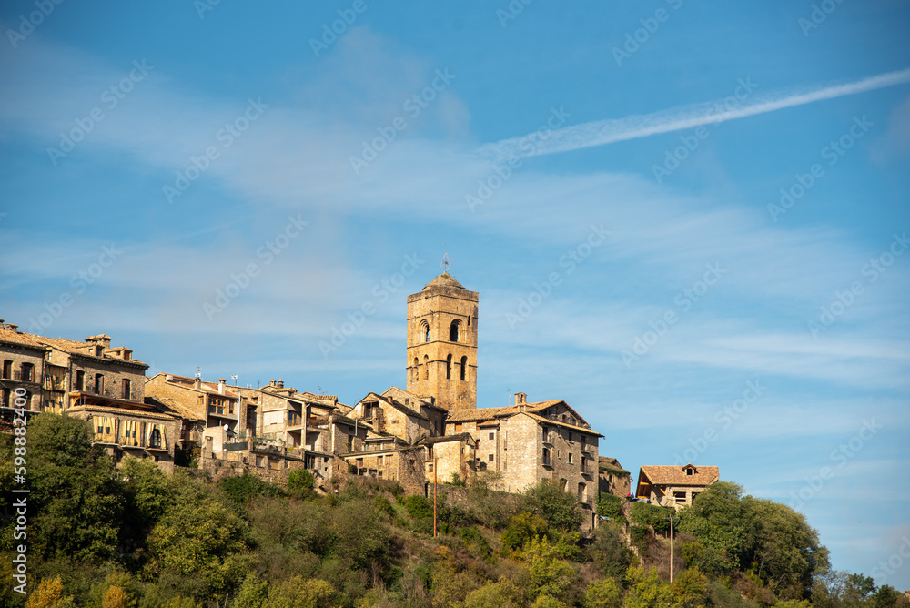 Panoramic view of the tourist town of Ainsa in Huesca, Aragon, with small brick and wooden houses and a large medieval style church in the upper part of the town on a hill on a sunny day.