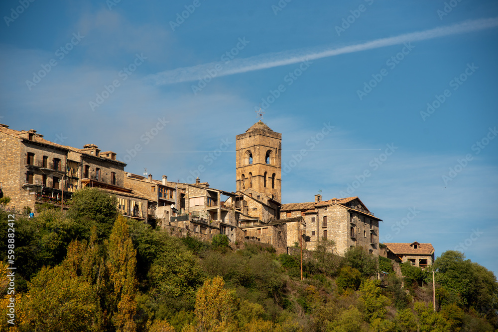 Panoramic view of the tourist village of Ainsa in Huesca, Aragon, made up of small brick and wooden houses next to a large medieval-style church, all surrounded by an impressive natural landscape.