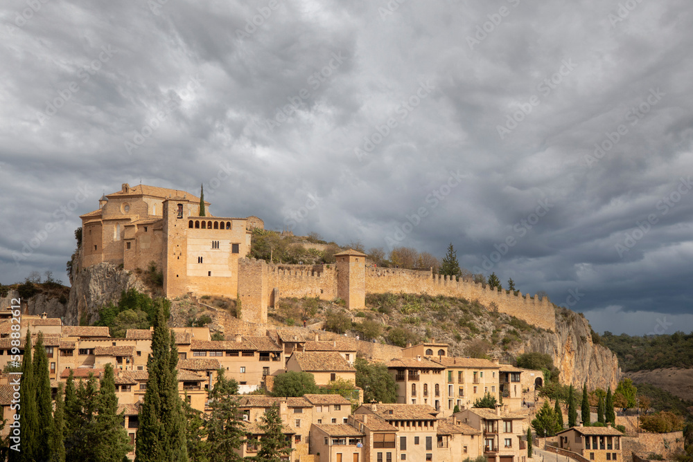 Impressive panoramic view of the touristy medieval village of Alquezar situated on a hill surrounded by mountains with small brick houses and a large walled church at the top.