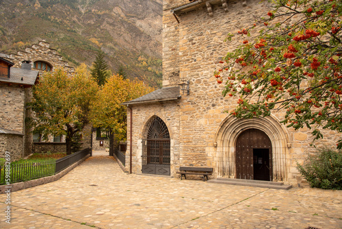 Detail plan of the stone portico of the church Santa María la Mayor next to a beautiful tree full of red fruits in the tourist village of Benasque, Huesca, Aragón.