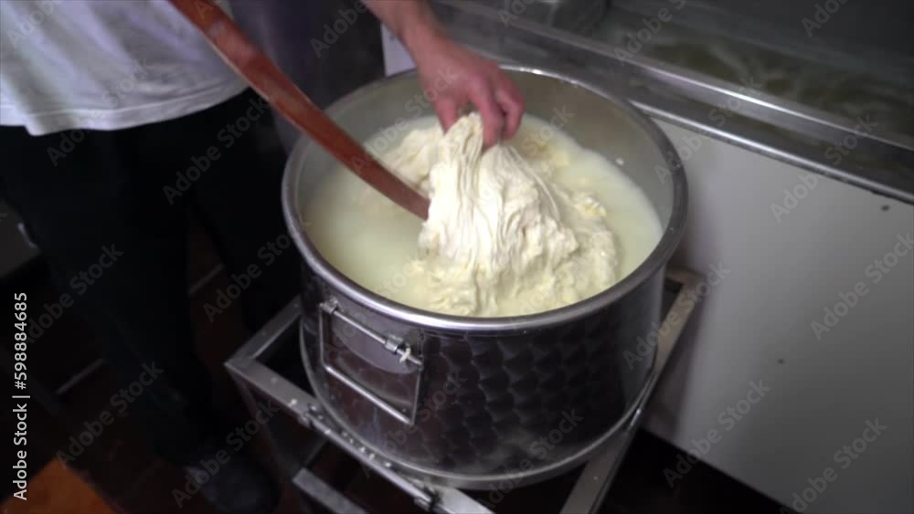 Mixing fresh cheese in a big pot of water with a large wooden shovel Mixing fresh cheese in a big pot of water with a large wooden shovel