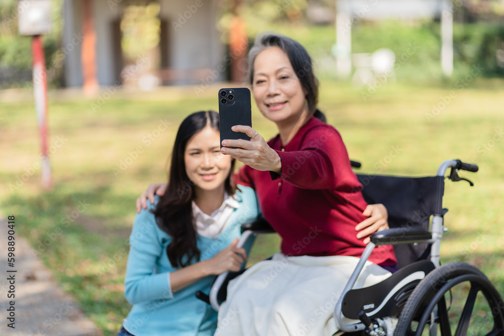 Asian senior woman in wheelchair with happy daughter. Family relationship retired woman sitting on wheelchair in the park age care at retirement home. Asian senior woman in wheelchair with happy daughter. Family relationship retired woman sitting on wheelchair in the park age care at retirement home.