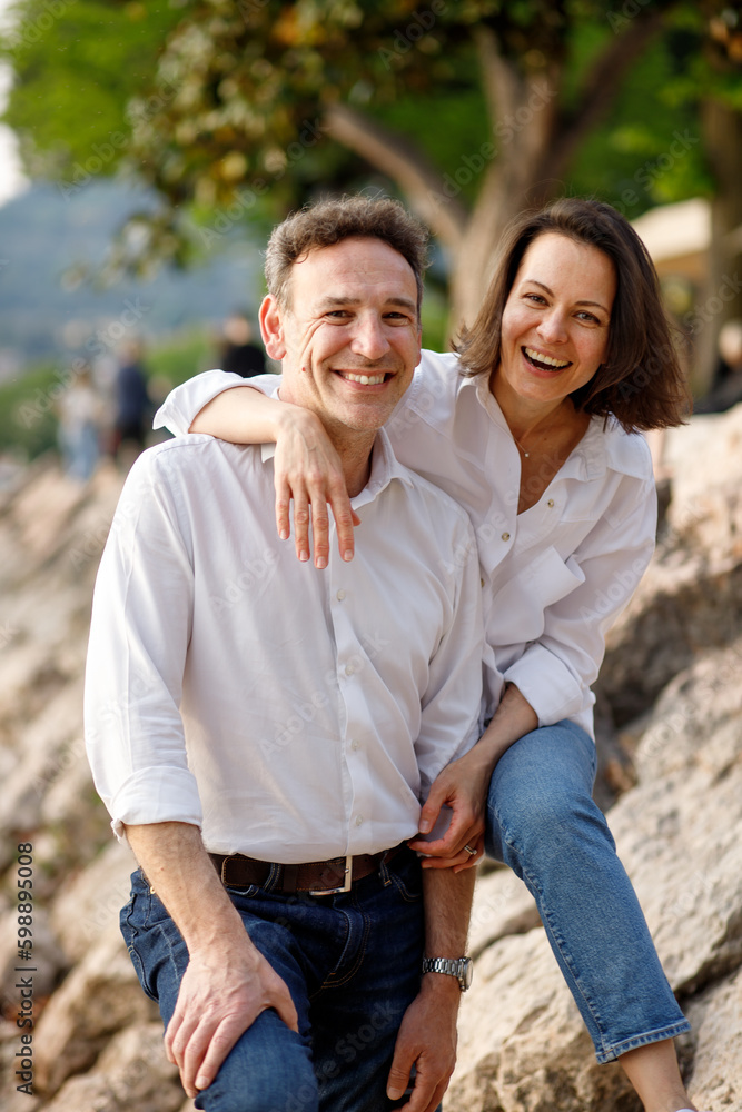 Portrait of stylish casual couple in love in white embracing each other at the Italian lake stone coast Portrait of stylish casual couple in love in white embracing each other at the Italian lake stone coast