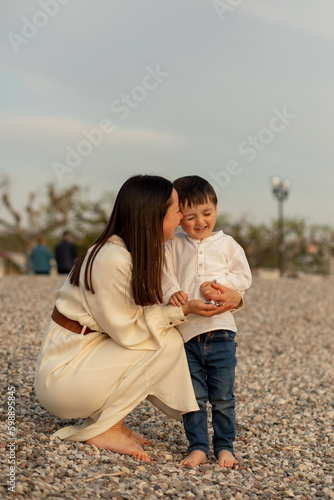 Brunette mom with sunglasses having fun smiling with her little toddler son at the Italian Garda beach at golden sunset 