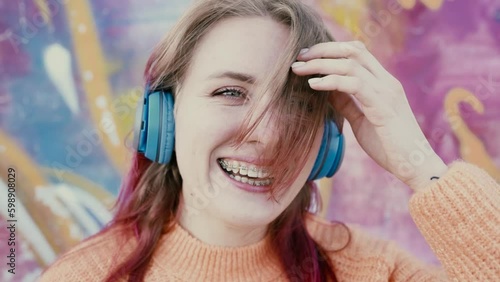Portrait of a young laughing girl with braces listening to music in headphones in the summer on the street